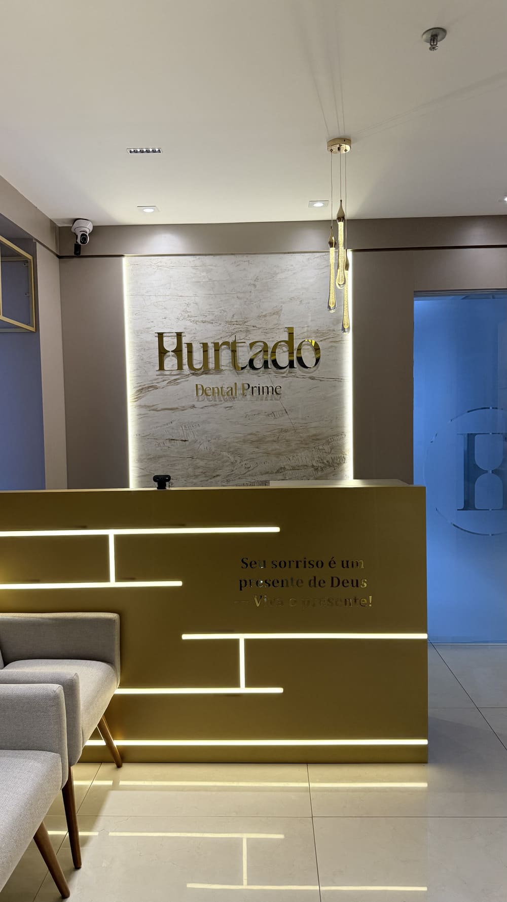 Recepção da clínica com painel de mármore, logotipo dourado e balcão dourado com frisos de luz