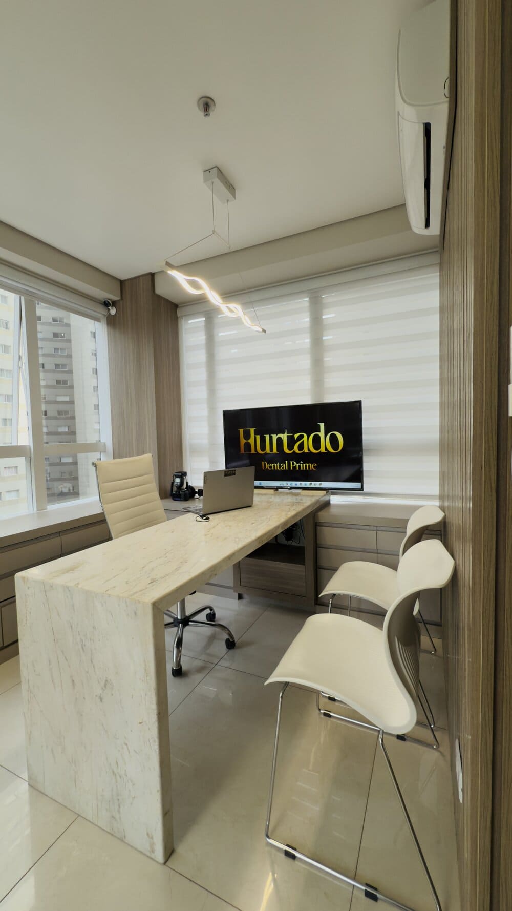 Sala de consulta com mesa de mármore, televisão exibindo o logotipo e janelas amplas